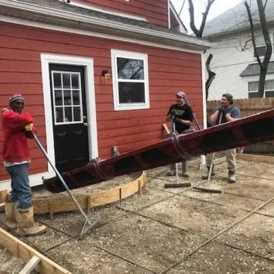Crew screeding fresh concrete for a back patio beside a red house