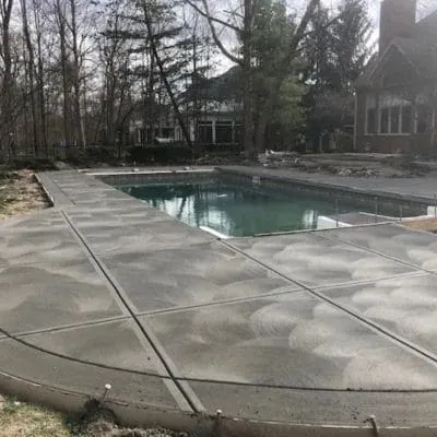 New broom-finished concrete deck around a rectangular pool in a wooded yard