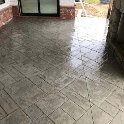 Gray stamped slate-pattern concrete porch floor beside a stone fireplace